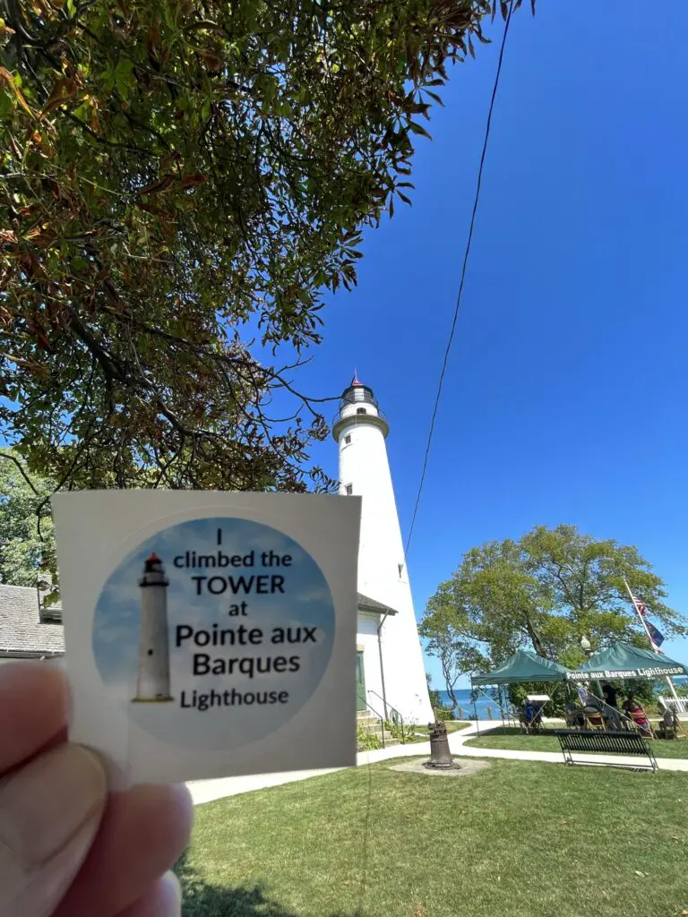 a hand holding a small white square with a lighthouse in the background