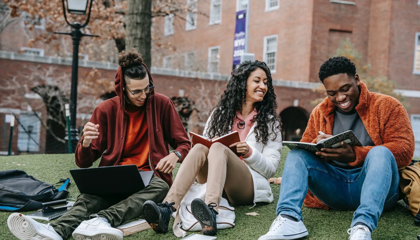 cheerful multiethnic students with books sitting near university - Featured image of diverse students at one of the best colleges in Michigan