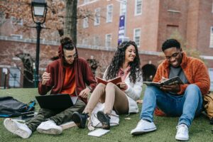 cheerful multiethnic students with books sitting near university - Featured image of diverse students at one of the best colleges in Michigan