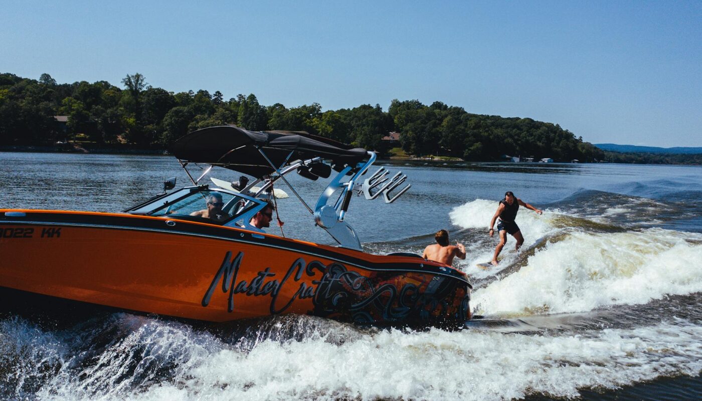 anonymous athlete on wake board near motor boat on lake