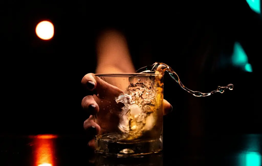 a hand holding a glass with ice and liquid