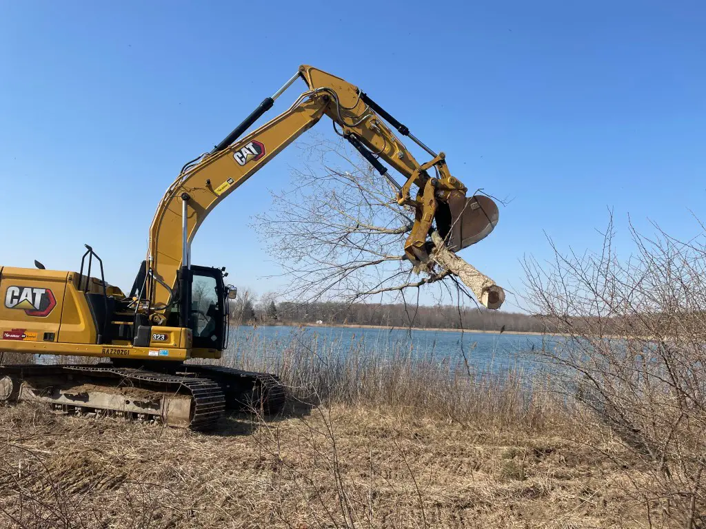 a yellow excavator with a bucket lifting a tree branch