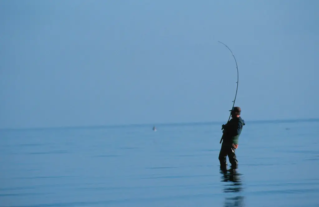 a man standing in water holding a fishing pole