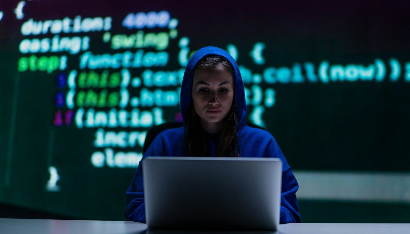 a woman in a hoodie sitting at a desk with a laptop