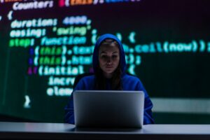 a woman in a hoodie sitting at a desk with a laptop