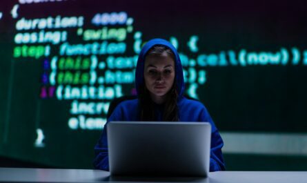 a woman in a hoodie sitting at a desk with a laptop