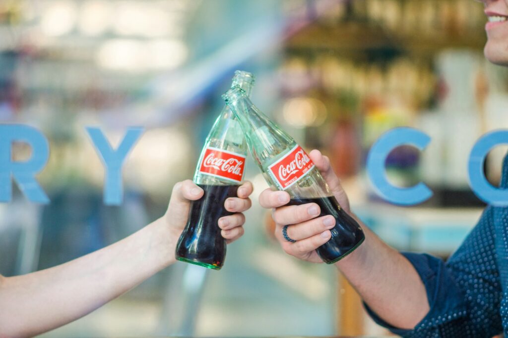 two hands holding bottles of soda