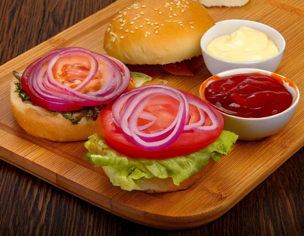 a burgers with onions and tomatoes on a cutting board