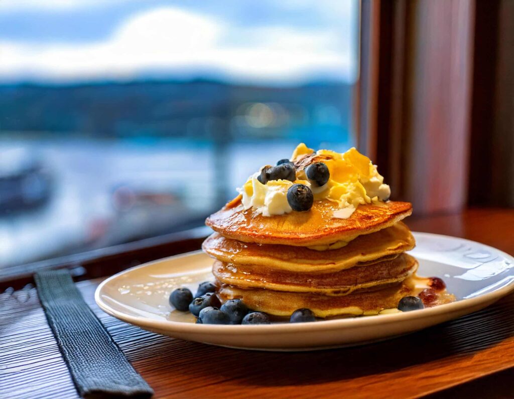 a stack of pancakes with blueberries and whipped cream on a white plate