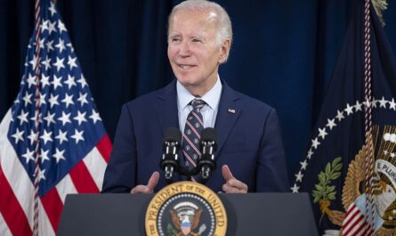 a man standing at a podium with flags behind him