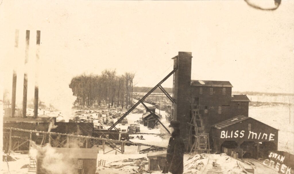 Black-and-white postcard view of the Bliss Coal Mine near Swan Creek, Michigan, showing mine buildings, smokestacks, conveyors, rail tracks and snow on the ground.