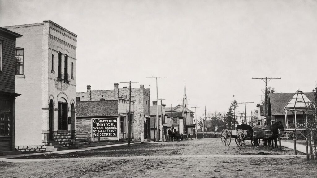 Historic view of downtown Caseville, Michigan, around 1900, with the Masonic Temple, Crawford drugstore, horse-drawn wagons and the Methodist Episcopal Church steeple.
