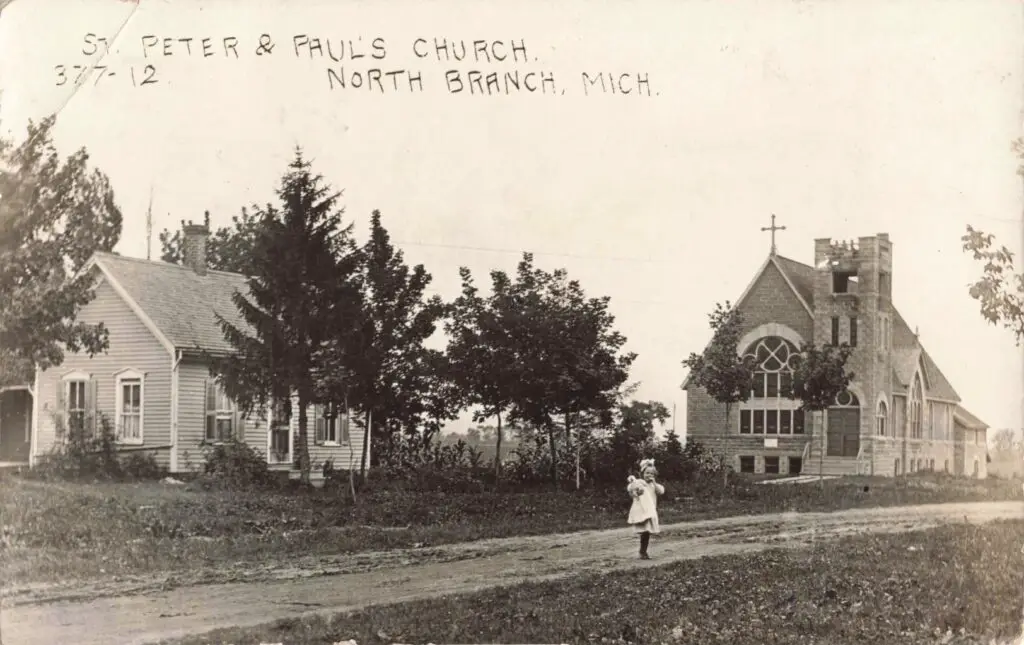 a child holding a baby in a white dress walking on a dirt road with trees and a church