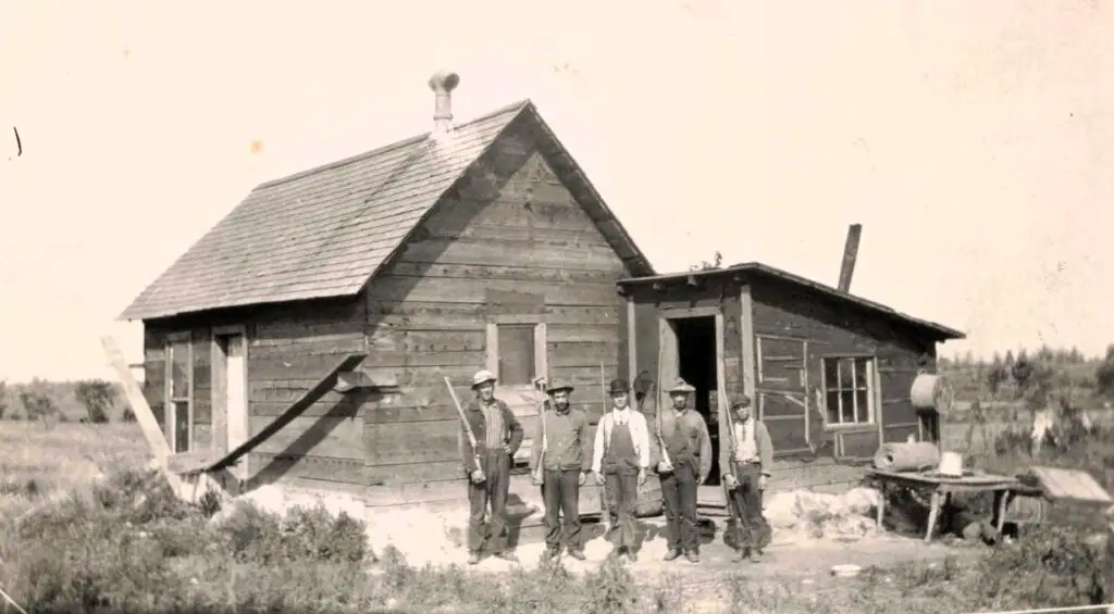 a group of men standing in front of a wooden house