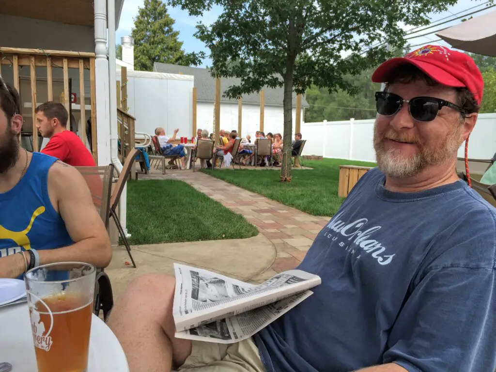 a man sitting outside with a newspaper and a man in a red hat