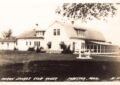 Black-and-white postcard photo of a large white clubhouse building with dormer windows and a long screened porch, set on a grassy lawn.