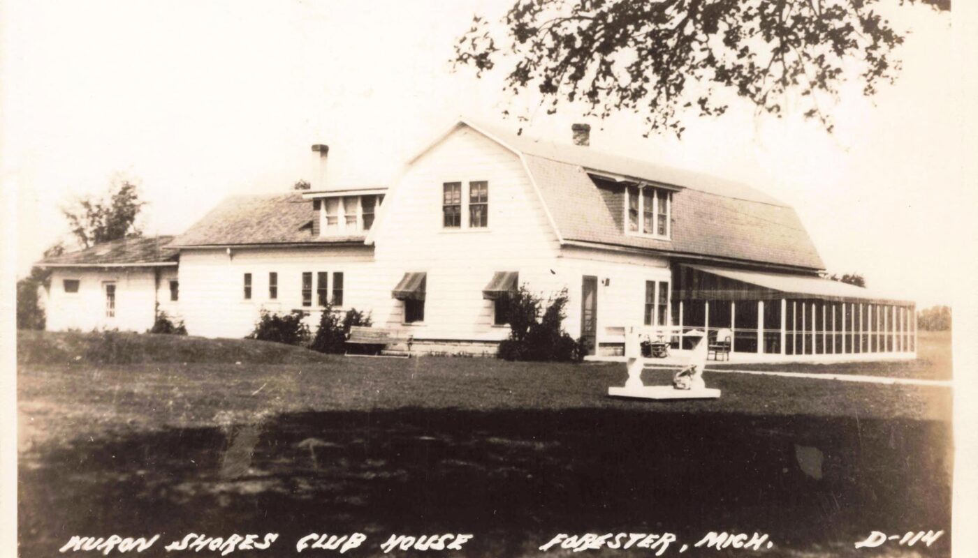 Black-and-white postcard photo of a large white clubhouse building with dormer windows and a long screened porch, set on a grassy lawn.