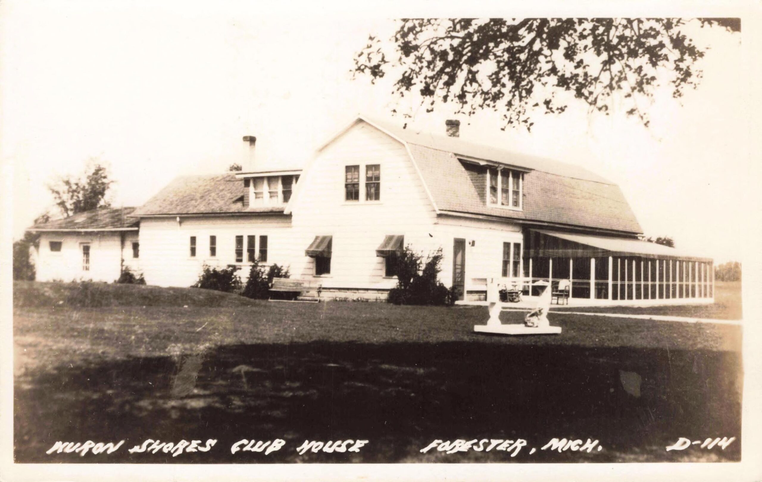 Black-and-white postcard photo of a large white clubhouse building with dormer windows and a long screened porch, set on a grassy lawn.