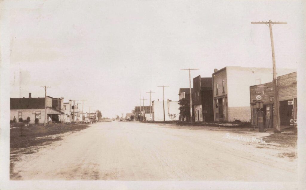 Main Street in Buckley, Michigan, in the early 1900s when dirt roads, wooden storefronts, and horse traffic defined daily life. Early gas pumps began appearing as automobiles slowly replaced horses. - The History of Buckley Michigan