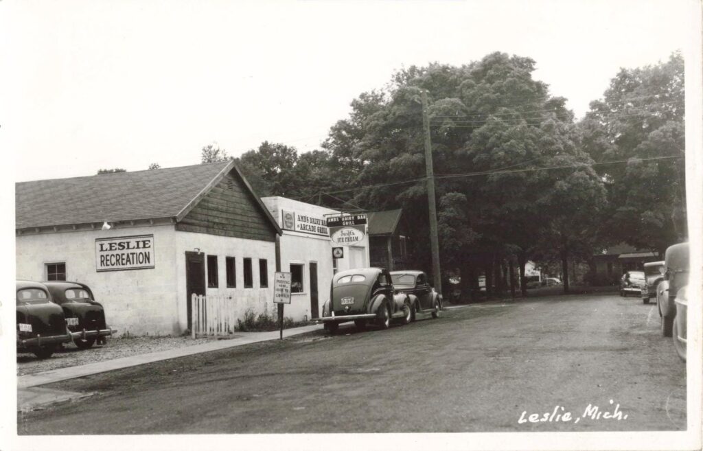 Vintage cars parked outside Ambs Dairy Bar and Leslie Recreation building in mid-20th century Leslie Michigan.