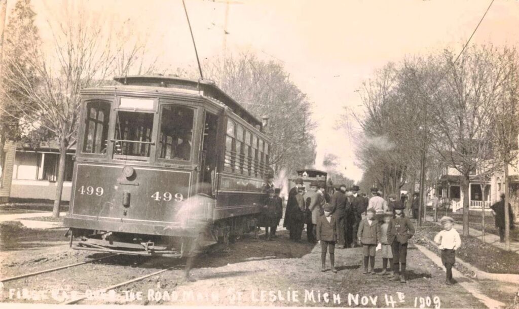Early electric streetcar in Leslie Michigan surrounded by residents during its first run in 1909.
