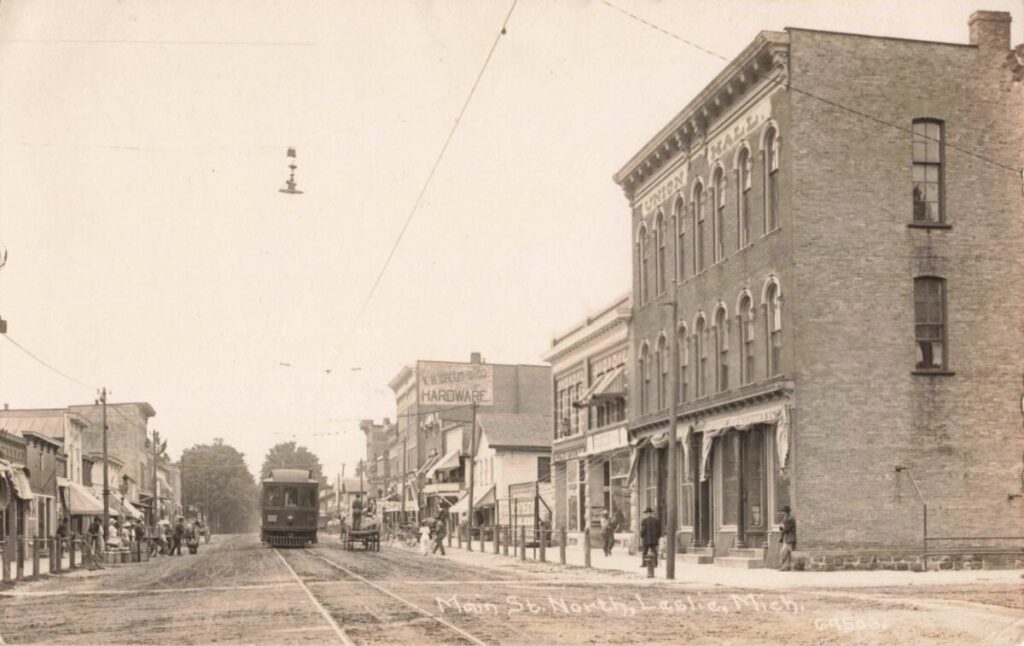 A sepia street scene shows an interurban railcar on tracks down Main Street with people, wagons, and a tall brick building marked “Union Block” on the right.