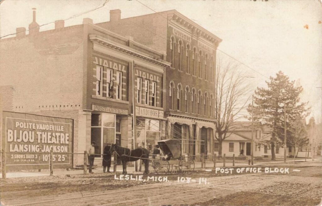A sepia street scene shows downtown Leslie with rail tracks in the road, a horse and buggy, and brick buildings labeled “Post Office,” “A.O. Du Bois,” and “Union Block.”