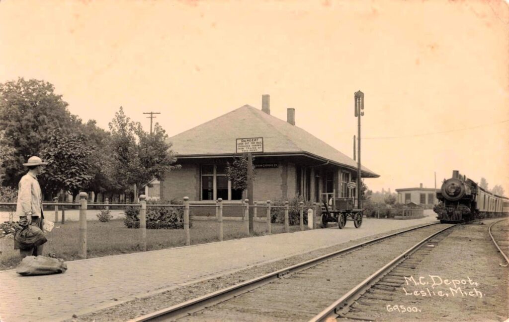 Early 1900s Michigan Central Railroad depot in Leslie Michigan with steam locomotive and platform activity.
