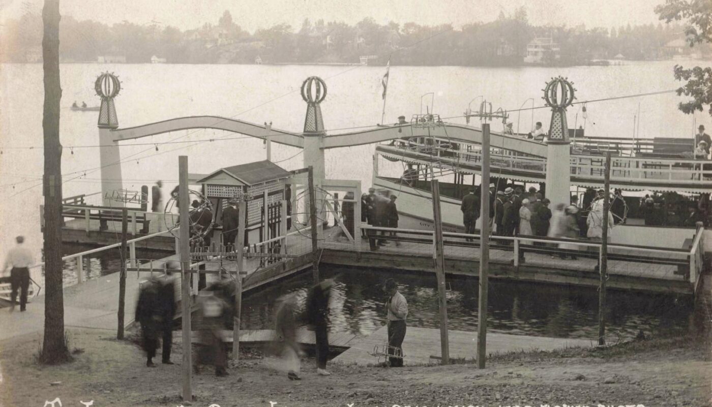 Black-and-white postcard photo of people boarding a two-deck passenger boat at the Park Island landing on Lake Orion, with docks and railings in the foreground.