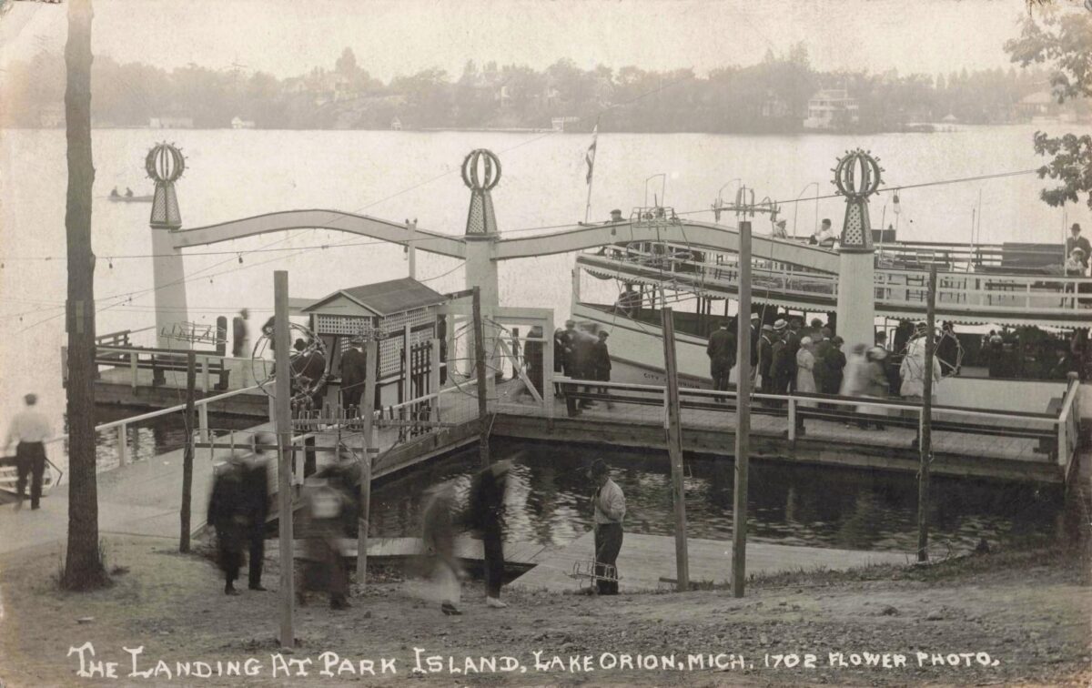 Black-and-white postcard photo of people boarding a two-deck passenger boat at the Park Island landing on Lake Orion, with docks and railings in the foreground.