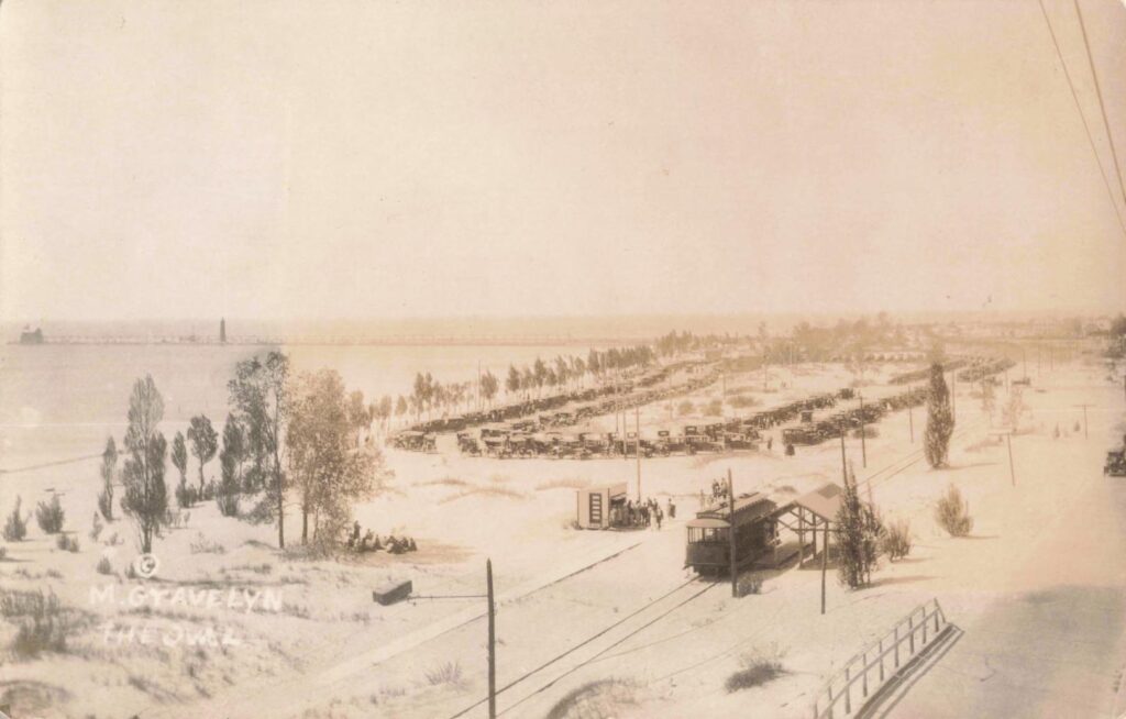Historic beach scene with vehicles and trees.