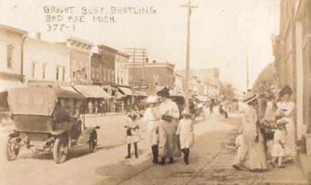 Early 1910s downtown Bad Axe Michigan showing dirt streets, wooden storefronts, wagons, horses, and early automobiles.