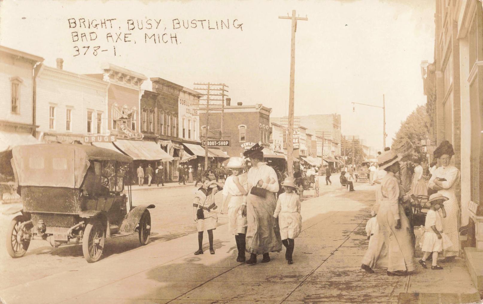 Early 1910s downtown Bad Axe Michigan showing dirt streets, wooden storefronts, wagons, horses, and early automobiles.