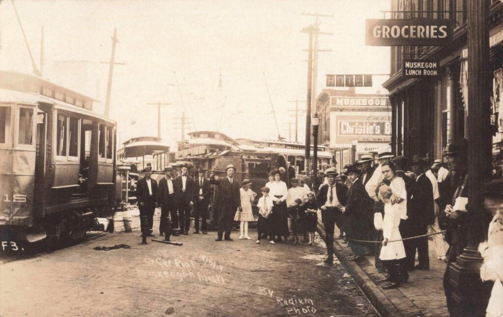 Large crowd gathered around damaged streetcars in downtown Muskegon during the Street Car Riot of 1919.