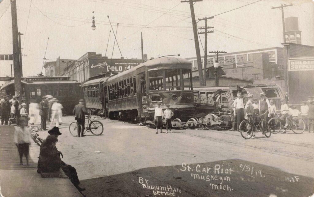 Streetcars wrecked and piled together in downtown Muskegon while crowds stand nearby during the 1919 riots.