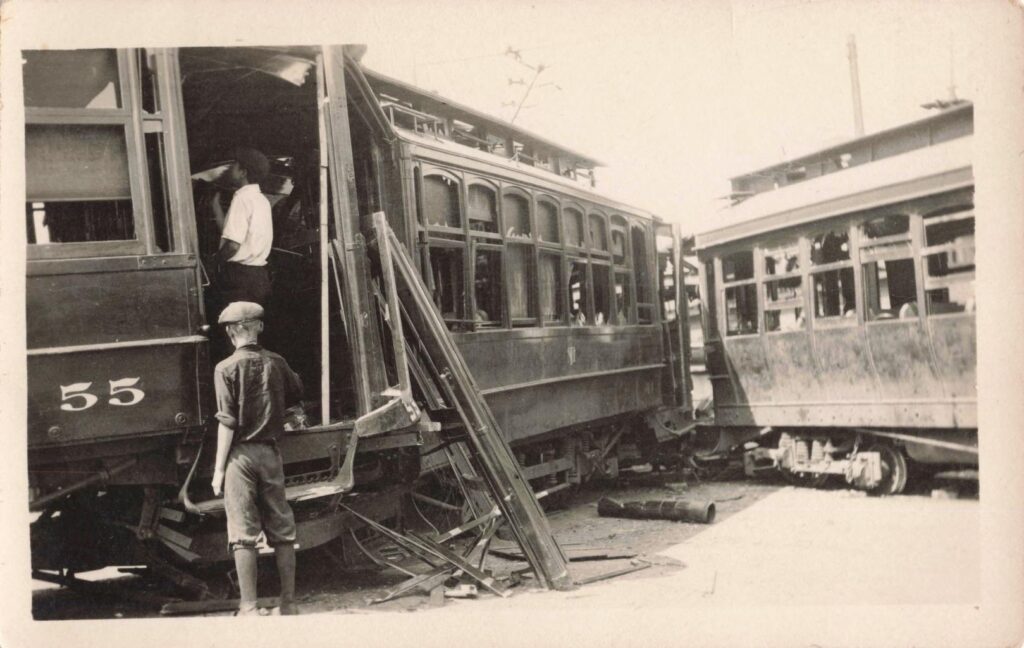Streetcars wrecked and piled together in downtown Muskegon while crowds stand nearby during the 1919 riots.
