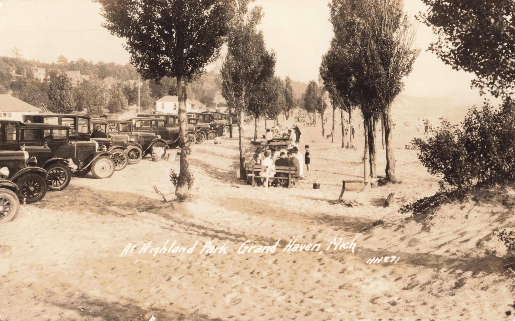 Vintage cars parked by sandy beach.