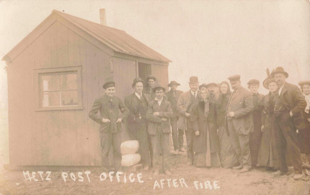 Metz post office after the fire, with residents gathered near a small surviving or temporary structure.