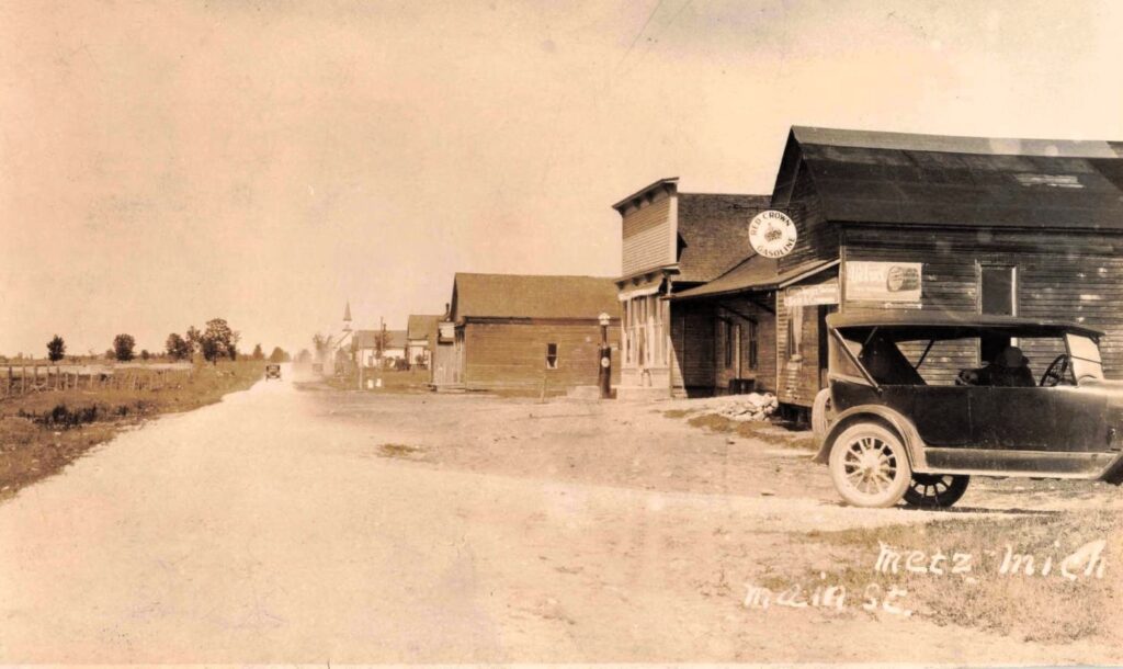  Street scene in Metz, Michigan, before the 1908 fire, showing the village’s stores, road, and railroad-era settlement pattern.
