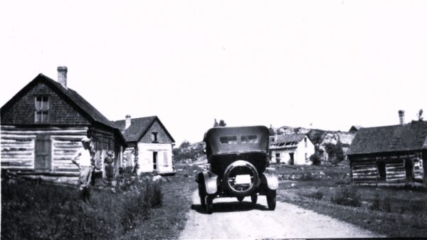 Old car on dirt road, rustic buildings