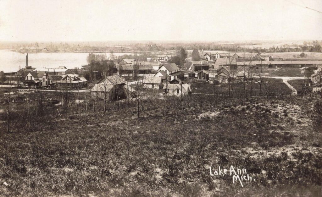 Lake Ann seen from higher ground, with the lake, village buildings and cleared land showing the town’s early scale.