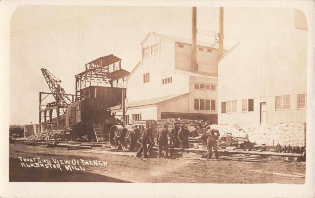 The new Alabaster mill rises after the 1910 fire, with workers and machinery gathered near the front of the plant.