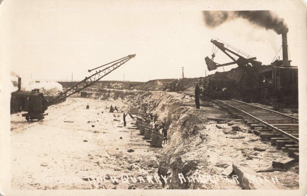 Workers and quarry cars stand among broken gypsum rock in a scene that shows the physical labor behind Alabaster’s early economy.