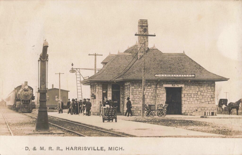 The Detroit & Mackinac Railway’s stone depot in Harrisville, around the early 1900s, with a steam train and gathered passengers