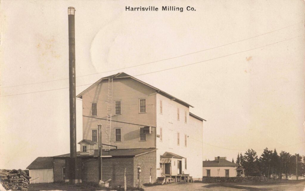 Harrisville Milling Co., pictured circa 1908, was a tall wooden mill building with a brick foundation and a towering smokestack.