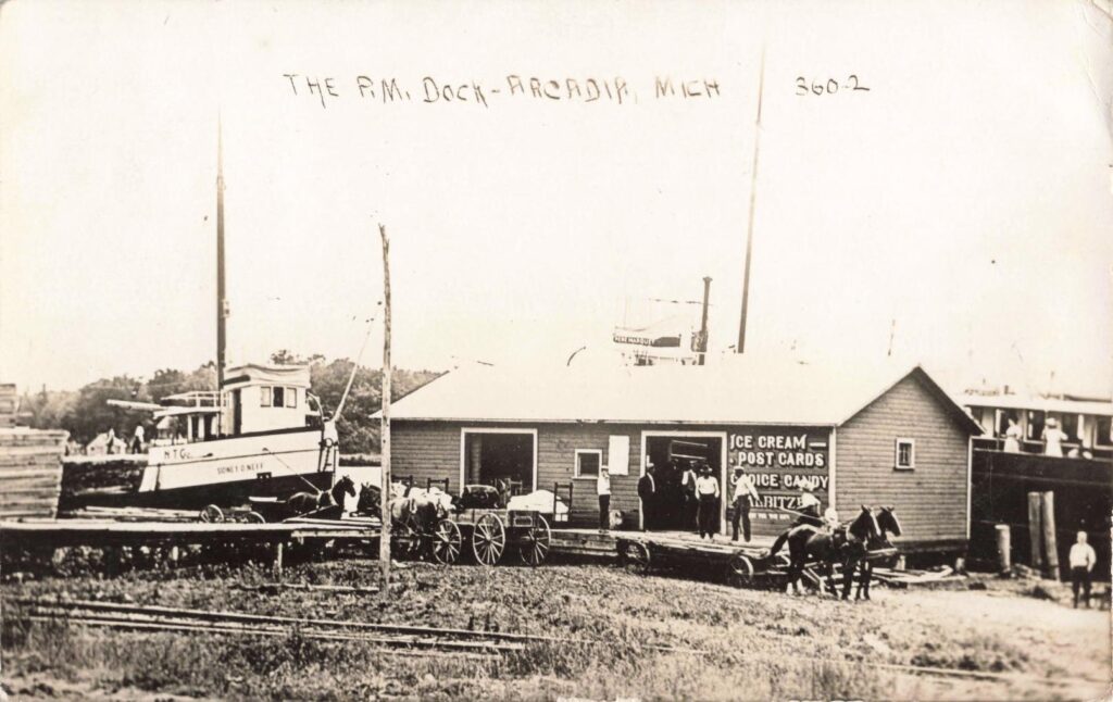 Pere Marquette dock, Arcadia, with a dockside store selling ice cream, postcards and candy. The view shows passenger traffic and small-town commerce beside freight work.
