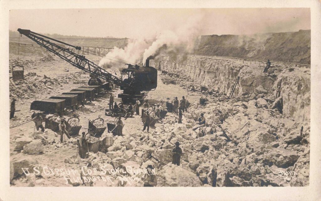 Gypsum Rock Quarry, Alabaster, Mich. - Workers and quarry cars stand among broken gypsum rock in a scene that shows the physical labor behind Alabaster’s early economy.