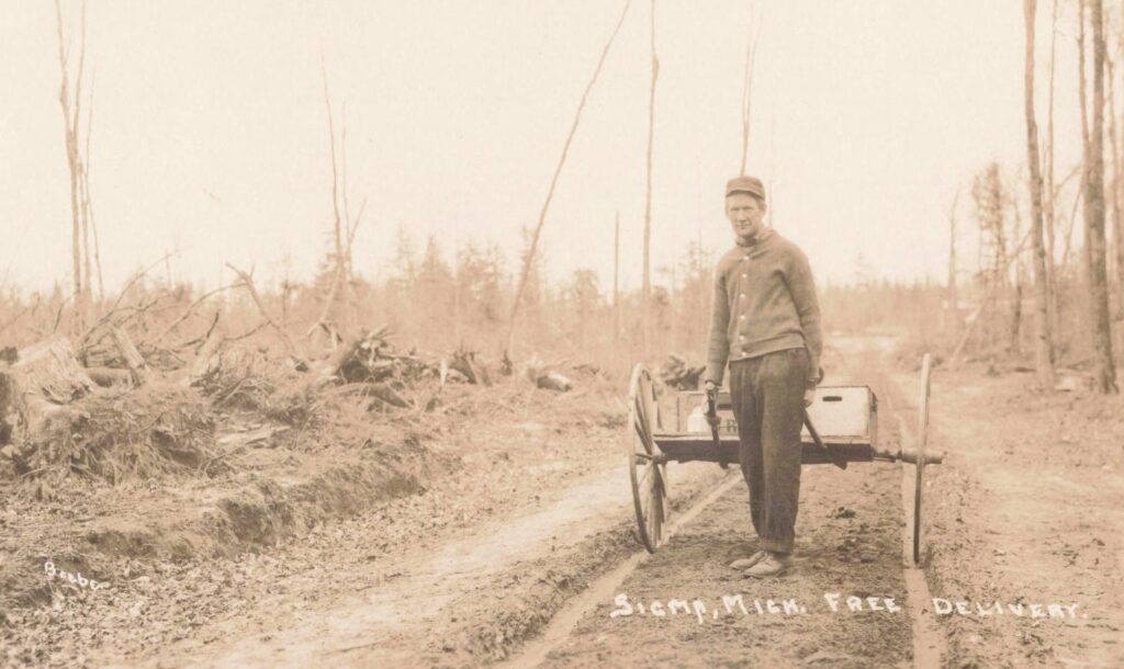 Free delivery cart, Sigma: A young man stands beside a simple delivery cart on a rough road, a reminder that even small lumber towns needed daily services to keep community life moving.