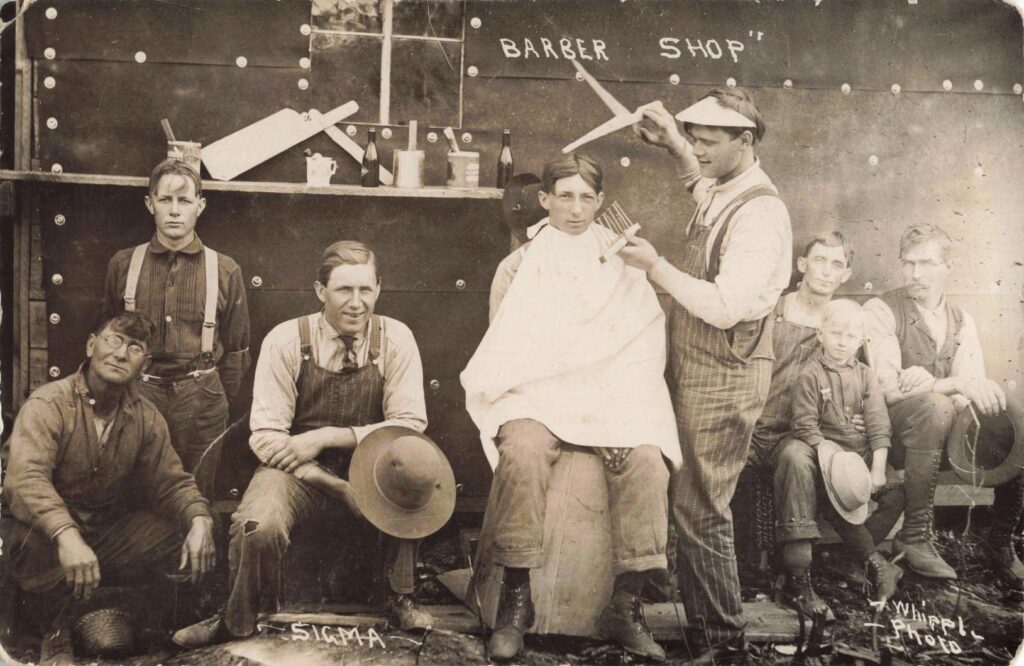 Barber shop scene, Sigma: Men and boys pose in a staged barber shop setting, a playful view that shows the humor and social life of a town often remembered only for logging.