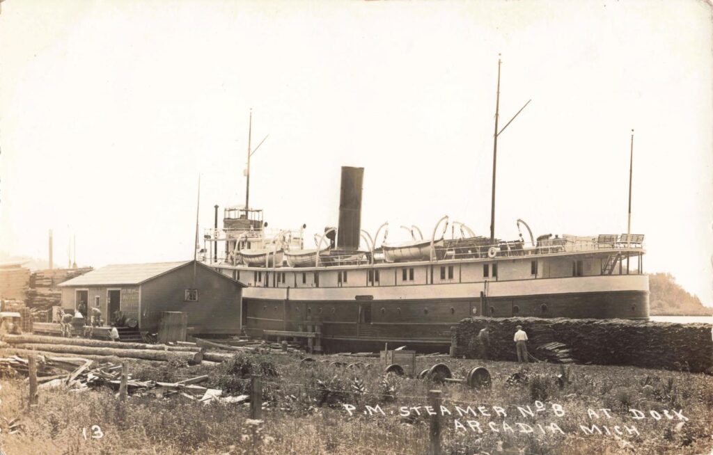 Pere Marquette No. 8 at Arcadia’s dock. Lumber piles and waiting people show the mix of freight and passenger service.